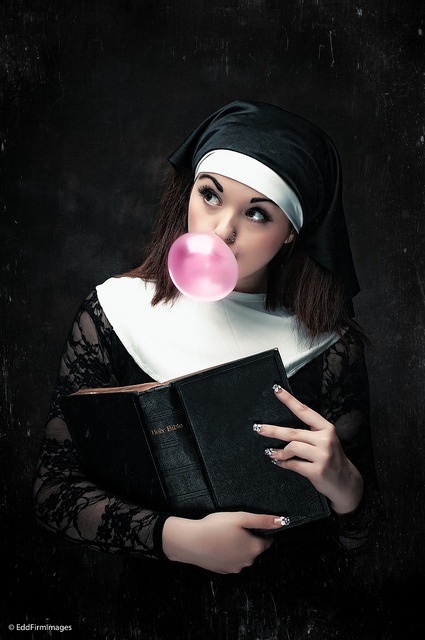Girl Wearing A Nun Outfit Holding A Book Whip Blowing A Bubble With Pink Bubblegum